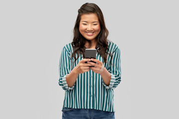 technology and people concept - happy asian woman using smartphone over grey background