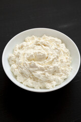 Tasty Ricotta Cheese in a white bowl on a black background, side view.