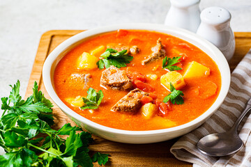 Soup with beef and vegetables in white plate on a wooden board. Traditional meat shurpa soup with vegetables and herbs.