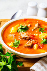 Soup with beef and vegetables in white plate on a wooden board. Traditional meat shurpa soup with vegetables and herbs.