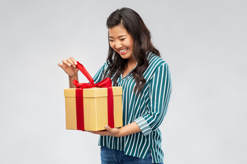birthday present and surprise concept - happy asian young woman opening gift box with red bow over grey background
