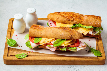Baguette sandwiches with meat, cheese and vegetables on wooden board.