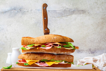 Baguette sandwiches with meat, cheese and vegetables on wooden board.