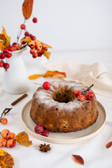 Homemade apple cake pie on white plate with fresh apples with leaves and cinnamon sticks on a light background. Side view, copy space for text. Bakery, confectionery, autumn recipies, desserts