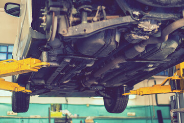 Car lifted in automobile service for fixing, worker repairs detail, telephoto. Car maintenance...