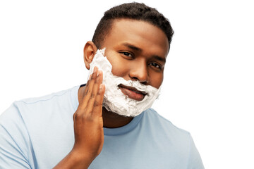 grooming and people concept - african american man applying shaving cream to his face over white...