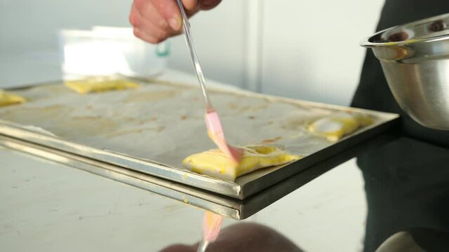 Lubricate with a brush the prepared mixture of raw dough for making buns, cookies. Baker male man makes fresh scone paste at table in bakery kitchen. Close up