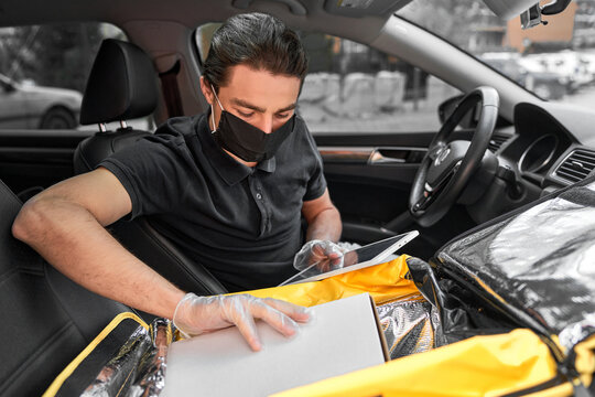 Smiling delivery man in protective mask and gloves driving a car delivered hot pizza from restaraunt to the customer. Fast online delivery around the city. Close up image