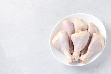 Raw chicken drumsticks in white plate on light gray background, Top view, Horizontal format, Space for text