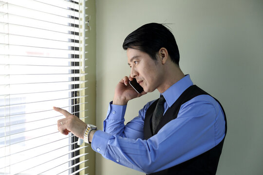 Southeast Asian Young Office Business Man In Formal Wear Looking Through Window Talking On Phone