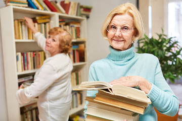 Fototapeta premium Lächelnde Seniorin mit einem Stapel Bücher in der Bibliothek für Wissen und Fortbildung