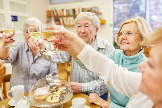 Gruppe Senioren stößt mit Weißwein an und feiert Geburtstag bei Kaffee und Kuchen