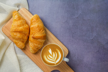 Croissants on wooden bread cutting board and latte art on cappuccino coffee cup with sackcloth over polished cement background. Croissant french breakfast. Top view.