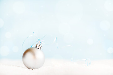 Christmas silver ball with ribbon on surface with snow and defocused lights with copy space