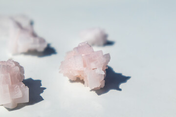 Fototapeta na wymiar Pink white salt flake crystals bunch on white reflective glossy surface. Spa resort crystallized ingredient bright close-up with selective focus