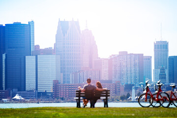 Lovely couple sit in the bench on Sunset Point over Detroit river and view of downtown on sunny day...