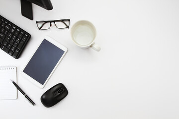 Personal computer, blank screen tablet, book and pen, eye glasses, and a glass of water. Top view, flat lay