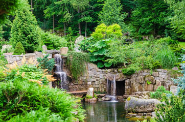 Japanese garden view of pond with waterfall, stone walls and shaped trees. Poland, Shklarska poreba.  Selective focus.