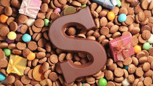 Rotation of kruidnoten, traditional sweets, strooigoed and milk chocolate letter S. Background for Dutch holiday Sinterklaas. St. Nicholas day concept. FullHD video, top view