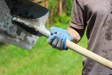 Dirty worker holds a shovel in his  hands under the scorching sun