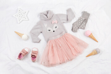 Set of casual child clothes, shoes and accessories on white background. Fashion girl lookbook consept. Knitted sweater, tulle skirt, sneakers, tights, ice cream cone. Top view, flat lay