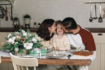 Happy family having fun with Christmas presents at home. Mom, Dad and beautiful daughter sit at the kitchen table at Christmas. Christmas holiday concept