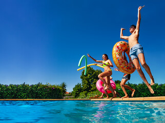 Many of happy teenage kids dive in the swimming pool water throw inflatable toys lifting hands have...