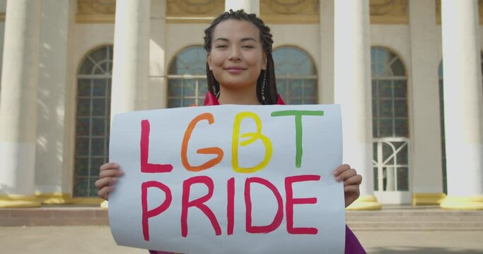 Smiling asian woman showing lgbt pride sign, covered with rainbow flag, equality