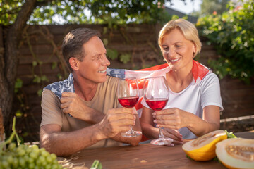 Smiling middle-aged couple sitting at table outside, toasting