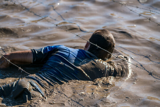 Athlete crawling in mud under barbed wire at an obstacle course race