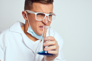 A laboratory assistant in a medical gown with a protective mask holds a flask with a chemical reaction liquid