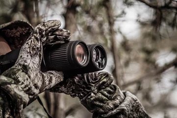 Poster hunter in a camouflage suit looks through binoculars on the hunt, close-up, soft focus © Евгений Мандажи