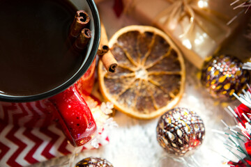 Red mug with tea and cinnamon sticks, a slice of dried orange, Christmas decor, gift boxes and garlands on the table. Flat lay. New Year