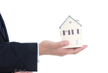 A person in formal wear holds a small house model in his hand