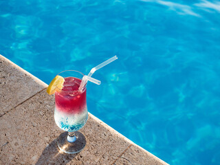 Beautiful cocktail glass on the background of the pool. View from above, close-up. Concept of leisure and travel