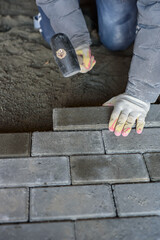 Man laying paving stones on the floor using a rubber mallet. Vertical