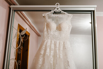 Beautiful classic lace silk wedding dress hanging on hanger in room. morning preparation wedding concept. vintage wedding gown.