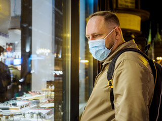 Adult man wearing mask walking in a night european city. Mask is a necessary thing in new normal...