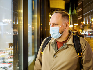 Adult man wearing mask walking in a night european city. Mask is a necessary thing in new normal...