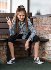 portrait of a beautiful teenage girl posing against a brick wall, show victory gesture