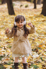 Portrait of a happy little girl listening to music on headphones in the autumn park