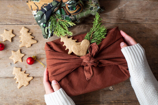 female hands in a white sweater are holding a Christmas present in a furoshiki package. zero waste concept. Ecological Christmas holiday concept, eco decor.