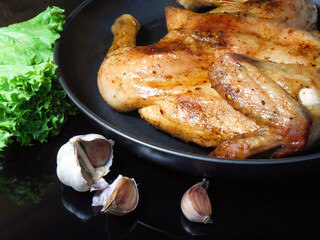 Fried roast chicken Tabaka in frying pan on black background.