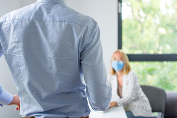 Work in a corporation during a pandemic. The man is giving a presentation and the woman wearing the face mask. Two business colleagues wearing protective face mask on a meeting during coronavirus.