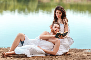 Fototapeta na wymiar caucasian couple wrapped in a blanket lie on the riverbank and read a book. Self isolation from people. Unity with nature and digital detox