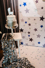 Birthday or baptism silver cake with figure carriage for a boy. Beautiful decorations for baby shower party near wall.