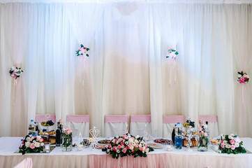 Festive tablen stands decorated with composition of pink flowers and greenery in the banquet hall. Table newlyweds in the banquet area on wedding party.