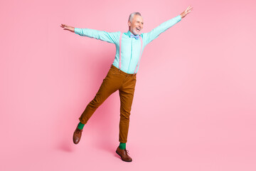 Full length body size photo of old man dancing keeping hands high pretending plane smiling isolated on pink color background