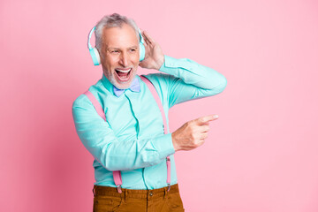 Portrait photo of happy grandfather listening to music with headphones singing song pointing with finger isolated on pink color background