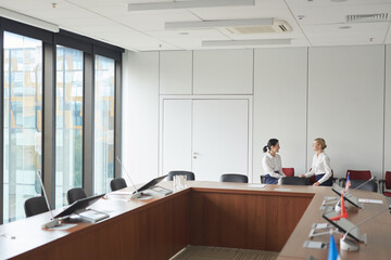 Wide angle shot of classic conference room interior with two female secretaries in background, copy...
